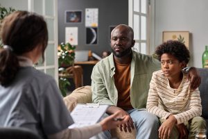 NDIS support worker with clipboard conducting an in-home assessment with a father and his young son during a family disability support consultation in Melbourne