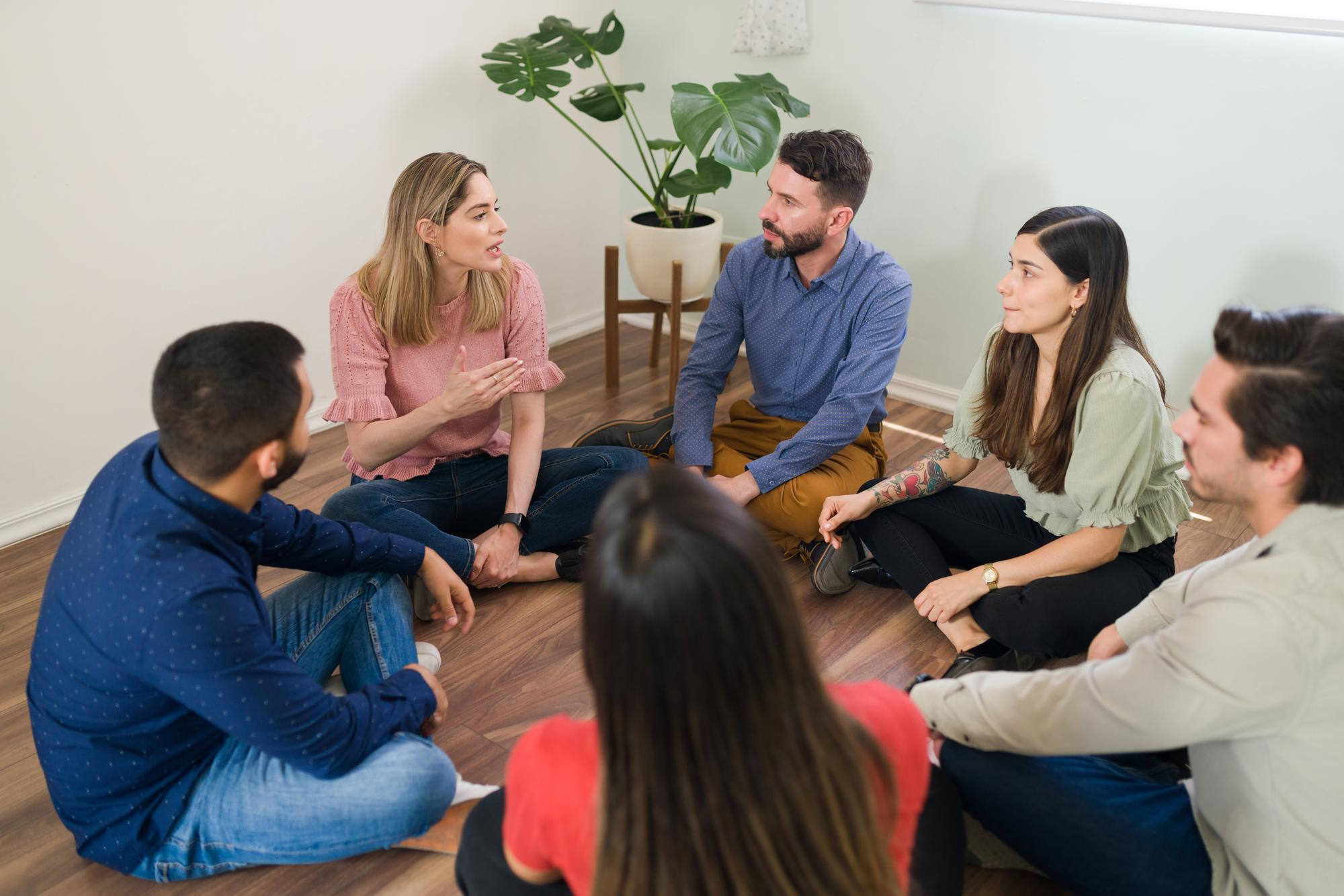 Diverse group of NDIS participants sitting on the floor in a circle sharing experiences during a mental health peer support and recovery session in Melbourne